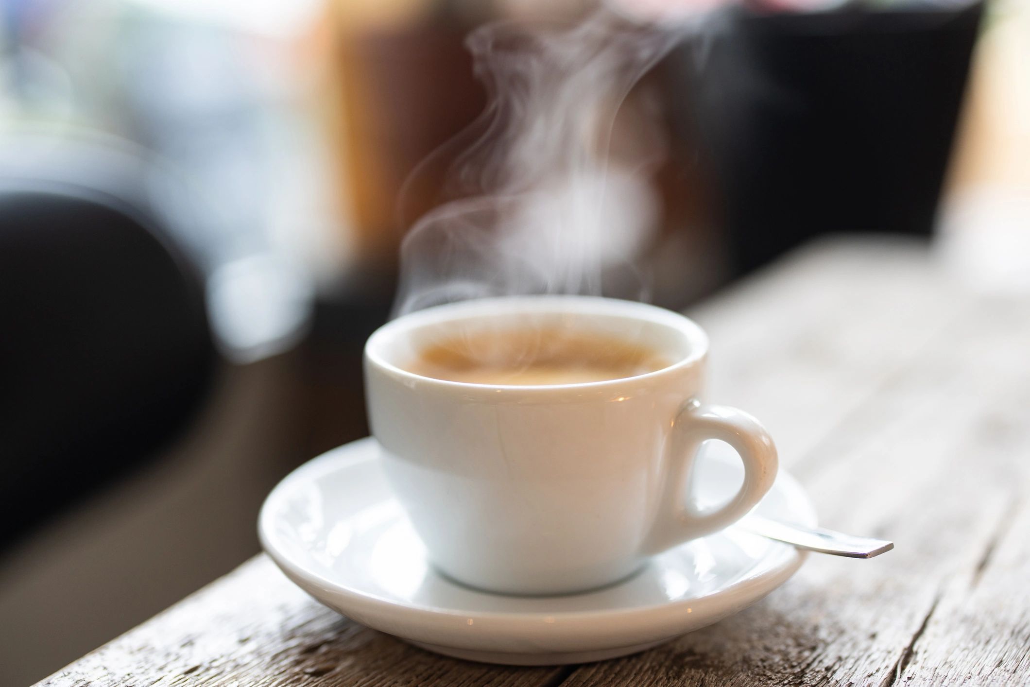 Steaming cup of hot coffee on a saucer on a wooden table